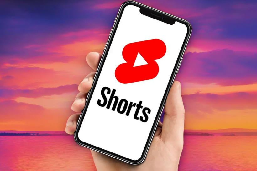 YouTube Shorts’a Uzun Videolar Ekleniyor! Akıllı telefon ekranında YouTube Shorts arayüzü ve arka planda bulanıklaşmış uzun formatlı bir YouTube videosu.
